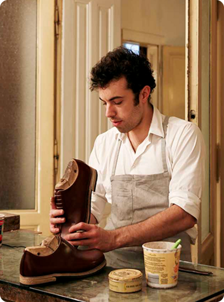 Male cobbler in overalls works on a pair of shoes in his shop