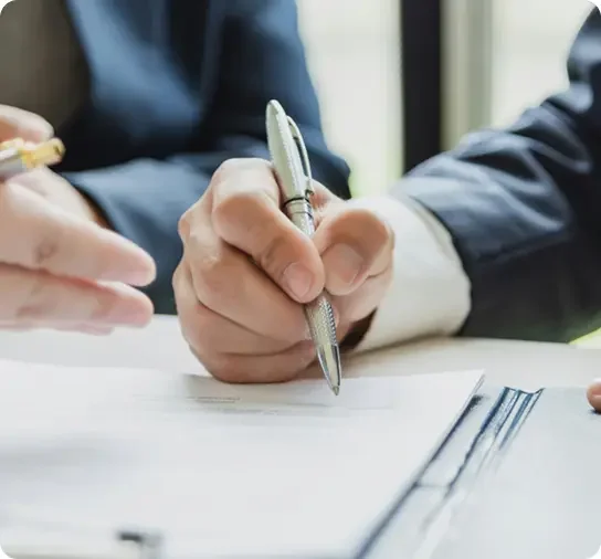 Close-up of two people in business suits reviewing and signing a document with pens