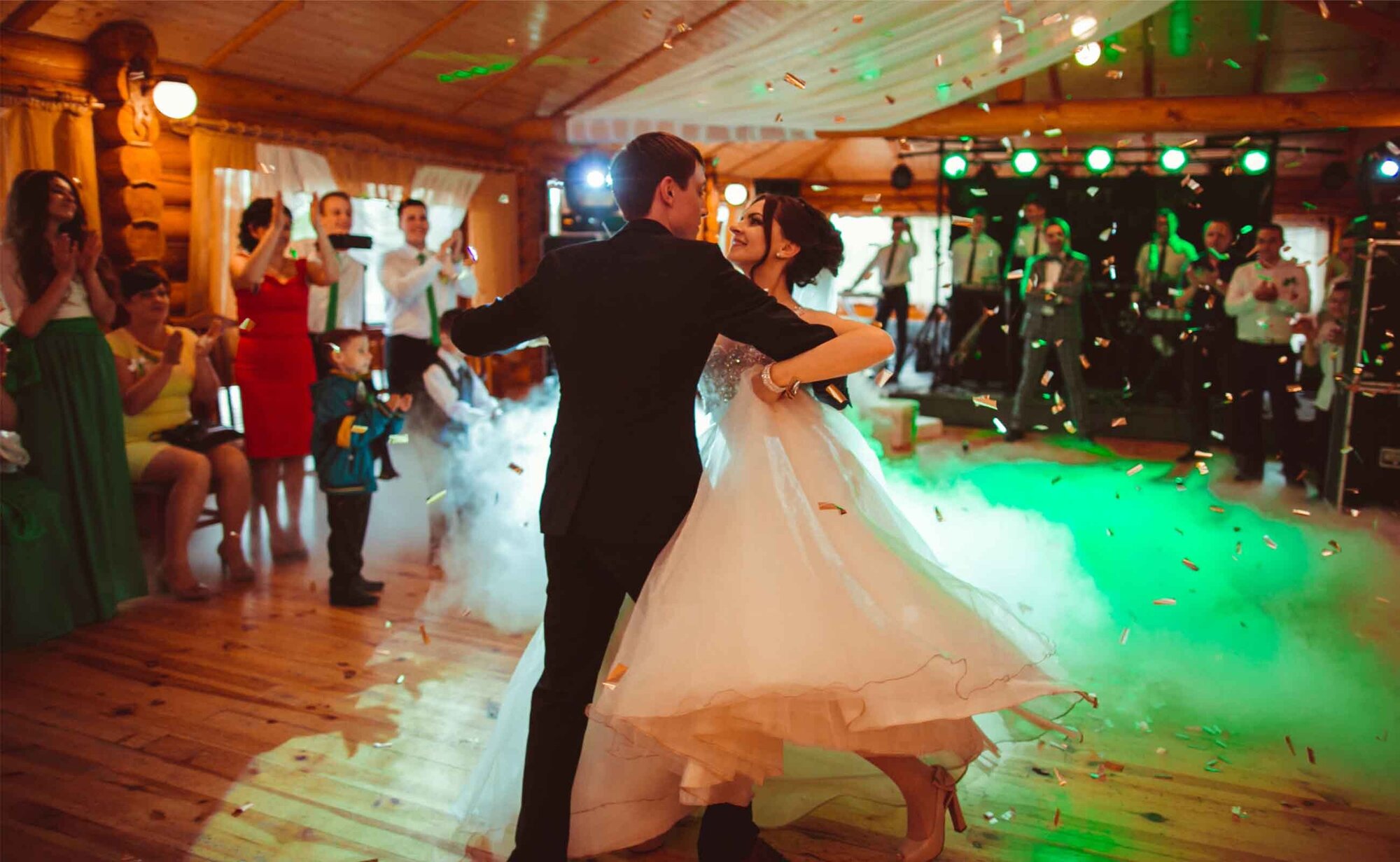 An image of a bride and groom dancing on the floor with smoke and confetti.