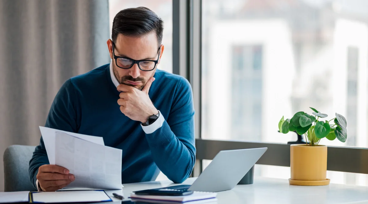 A man reading notes and looking at his laptop.