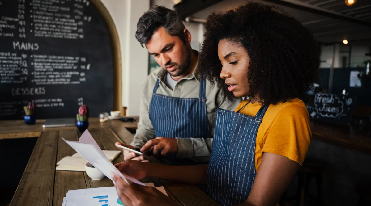 Two people in aprons reviewing documents in a cafe