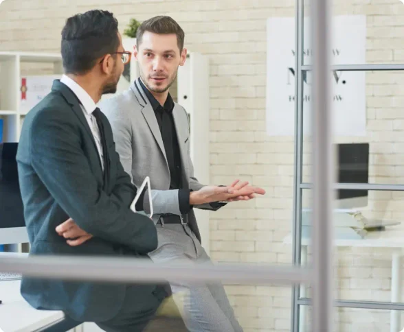 Man wearing a grey suit with a black shirt talking to a male coworker in a black suit with white shirt and black tie discussing doing their business dissolution with LegalZoom.