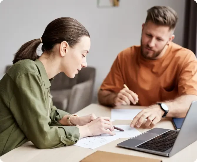 Brunette white woman with her hair in a pony tail wearing a long sleeved green blouse sitting next to a brunette White man wearing a orange shirt sitting in front of a laptop discussing their LegalZoom business dissolution.