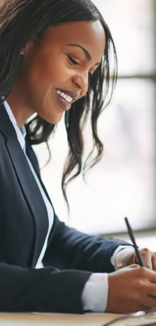 An attorney taking notes at a table on what her client's employment agreement needs to contain