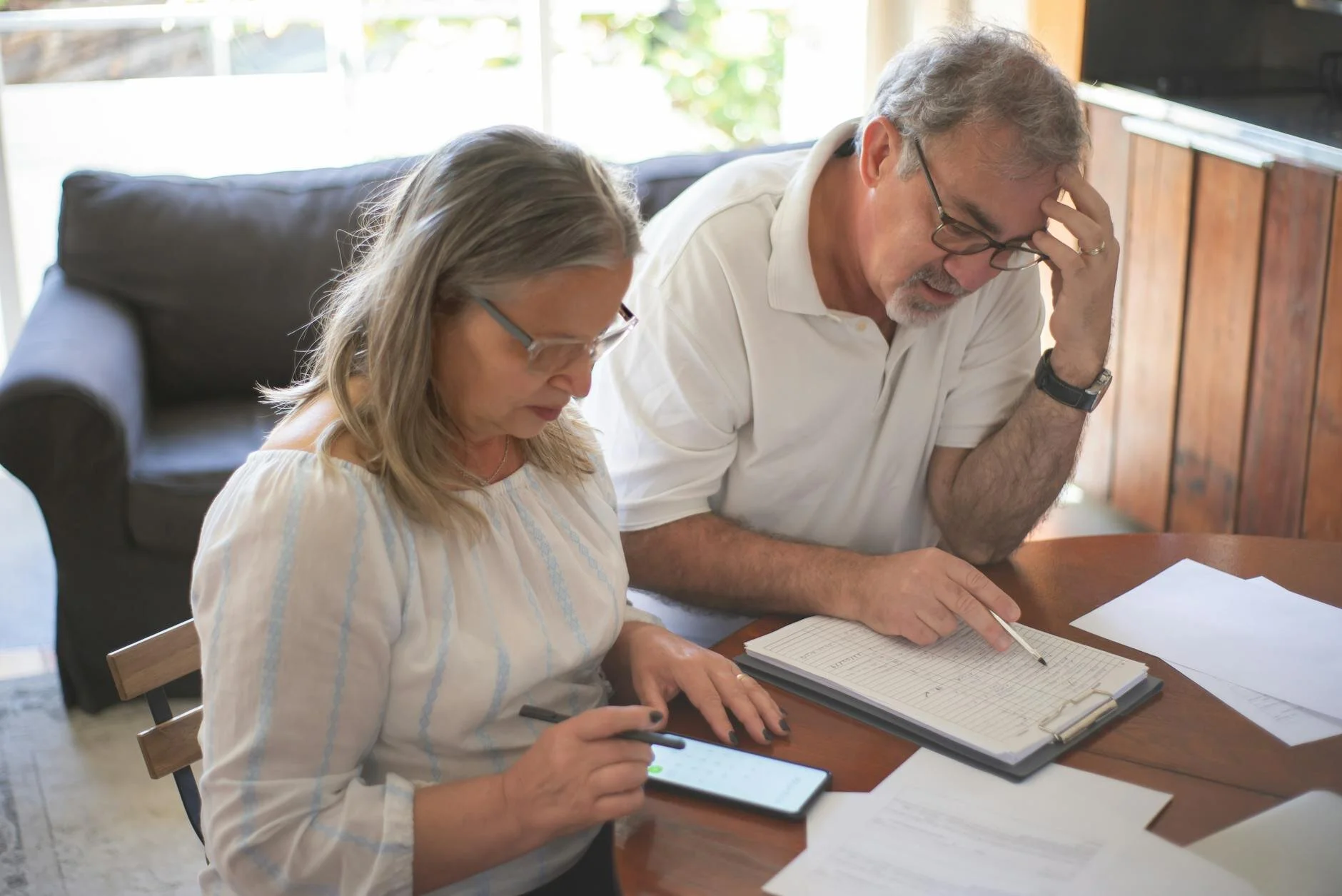 An elderly couple seated at a table takes notes on estate planning and discusses the types of assets covered in Florida, which include real estate properties, bank accounts, financial assets, vehicles, and personal belongings.