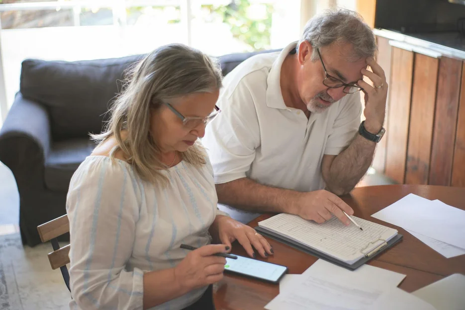 An elderly couple seated at a table takes notes on estate planning and discusses the types of assets covered in Florida, which include real estate properties, bank accounts, financial assets, vehicles, and personal belongings.