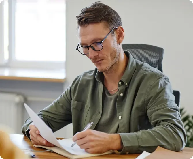 Brunette White man with a 5 o'clock shadow and glasses wearing a green button up shirt on top of green t-shirt filling out the dissolution paperwork that he received from LegalZoom.
