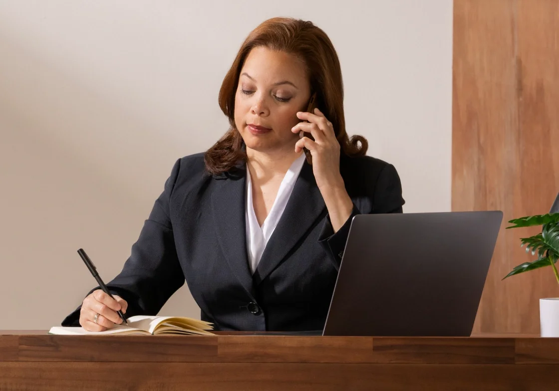 woman sitting at her desk making a call and taking notes.