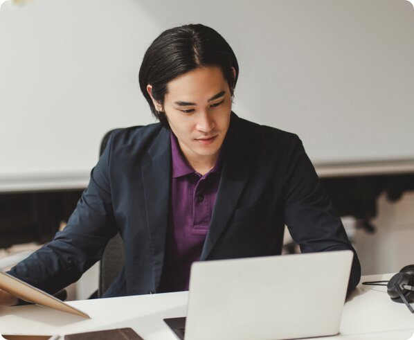 Asian man wearing a black suit jacket over a purple collared shirt working on his LegalZoom business dissolution on his laptop.