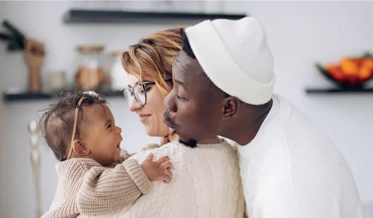 a couple wearing white hold their baby and smile