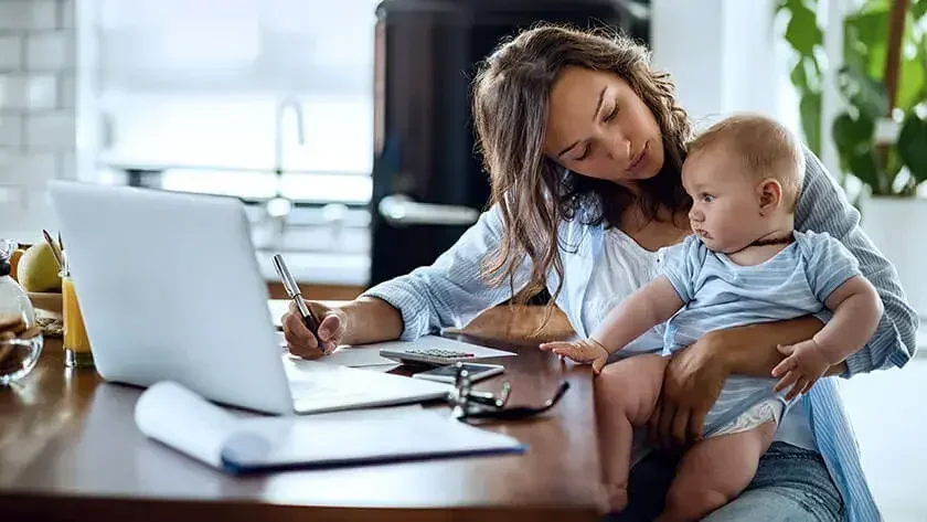 A mother working at home holding a baby.