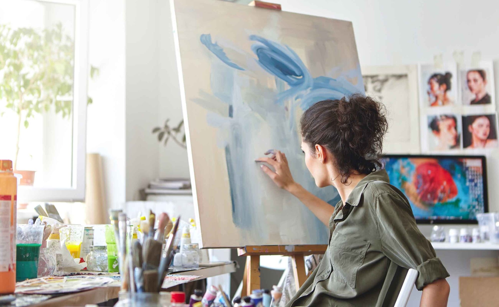 An image of an artist painting on a canvas in her workspace.