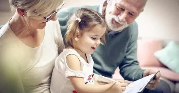 Two grandparents hold their preschool-aged granddaughter and encourage her while she practices handwriting.