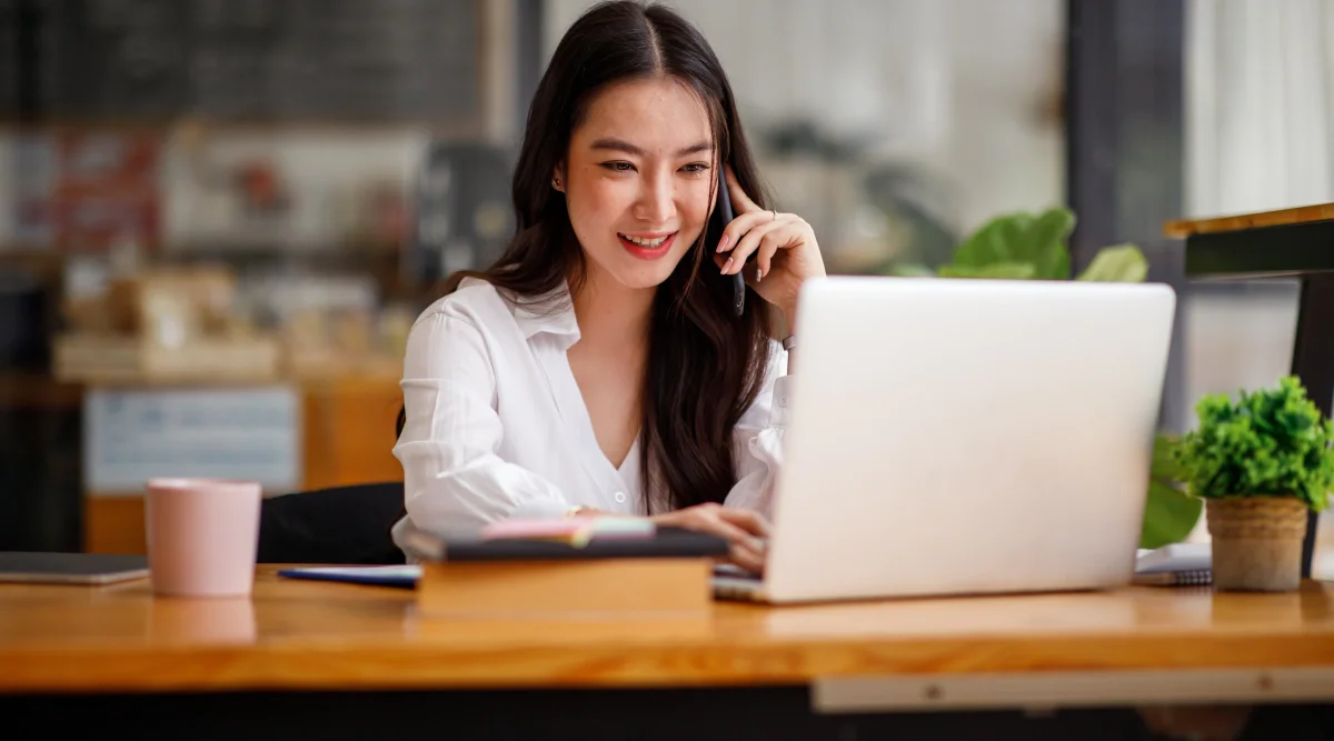 Woman on a call, smiling while using a laptop in a cafe