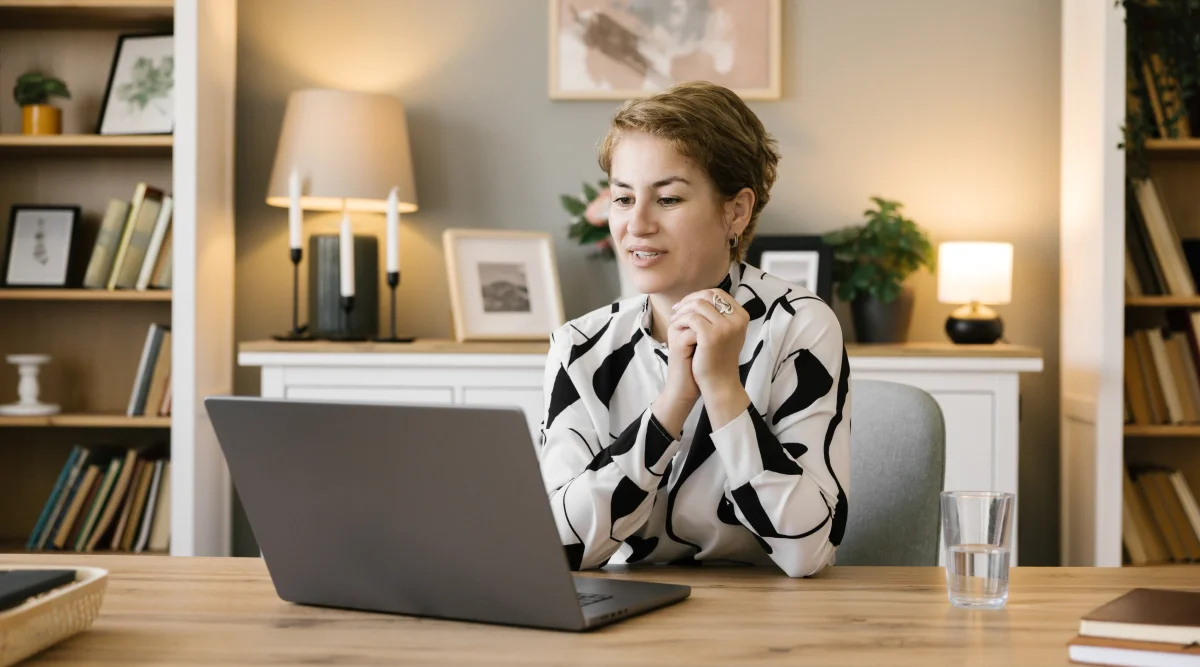 Woman in patterned shirt writing, near monitor