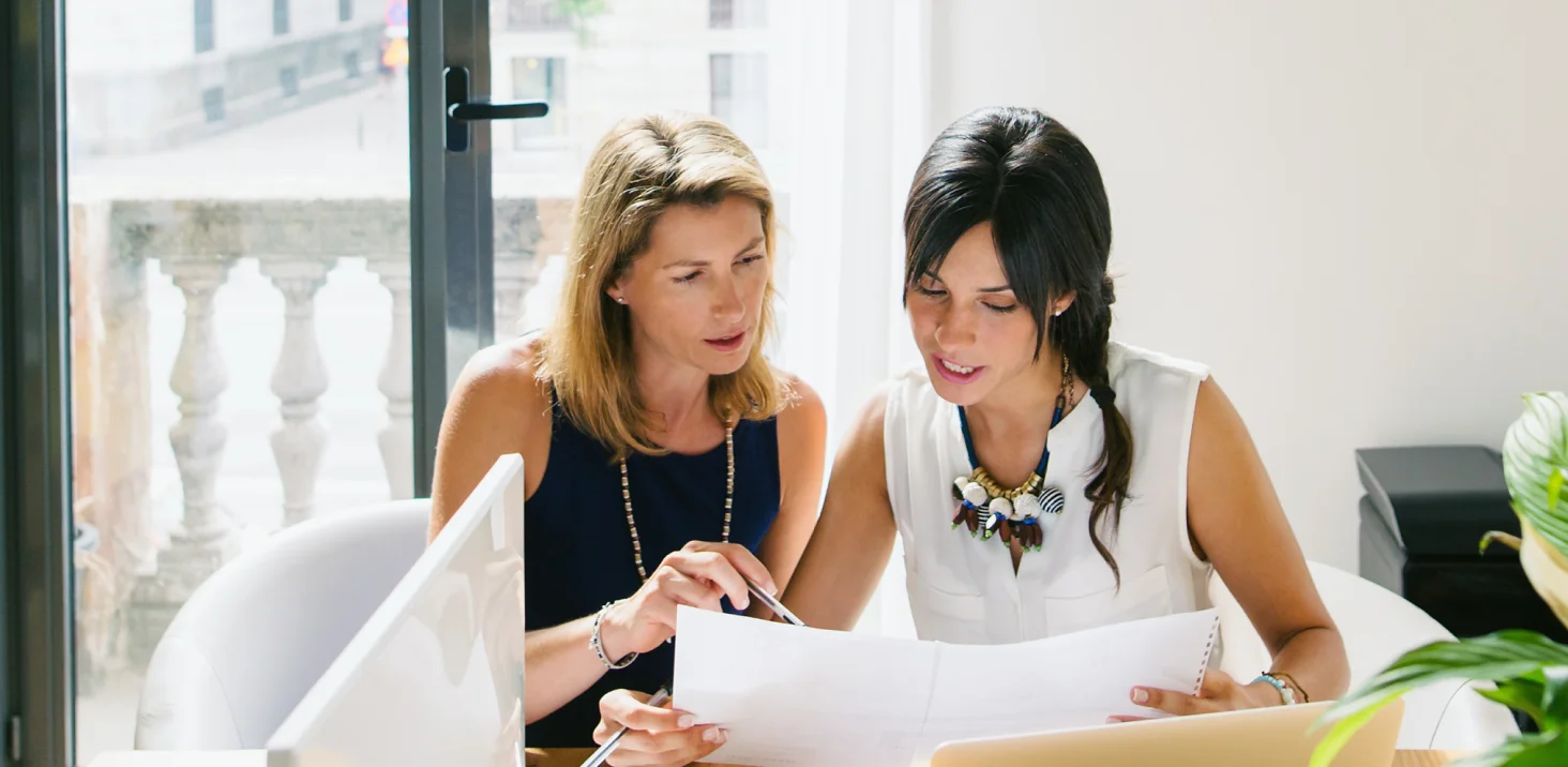 Two women discuss items on pieces of paper