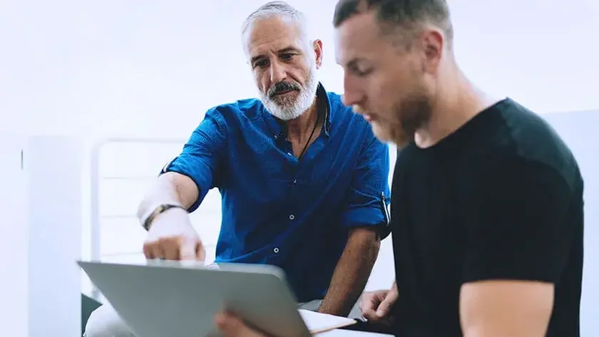 Father sits with his son going over items on their laptop.