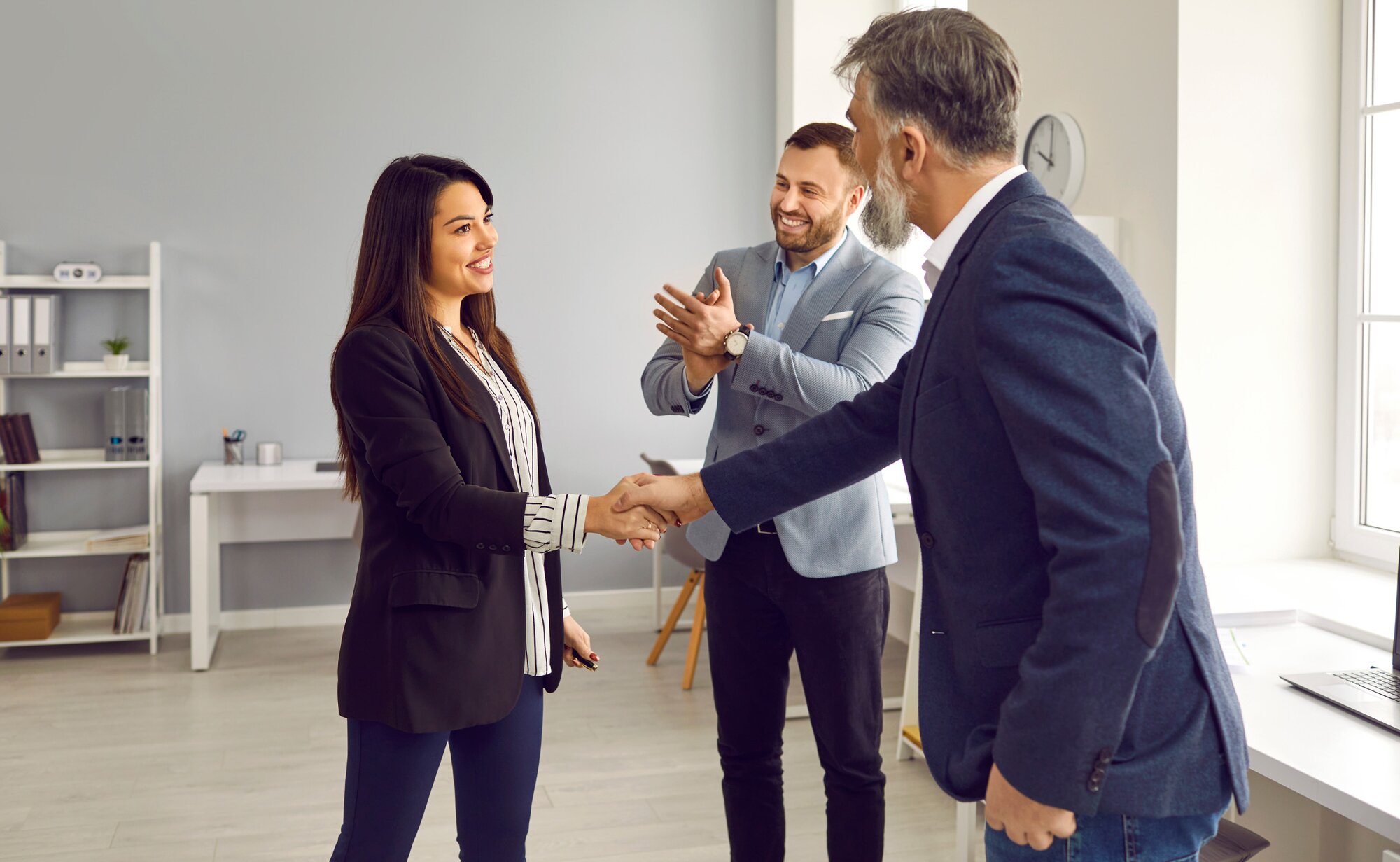 A male employee congratulates a female employee in an office while others are clapping. 