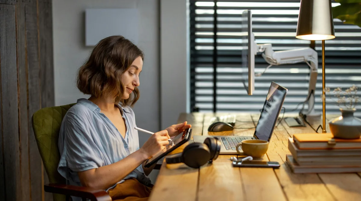 Woman using stylus with laptop at wooden desk