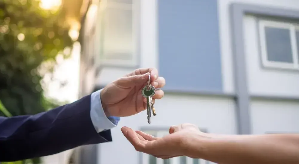 hand of the person passing keys to another person in front of the house