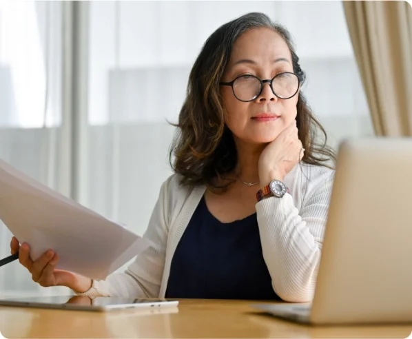 A woman wearing glasses sits at her computer thoughtfully.
