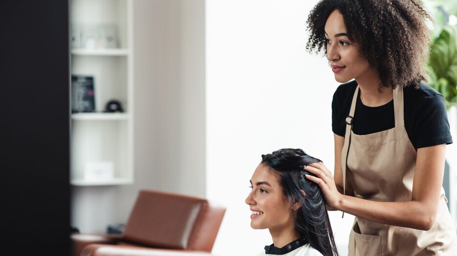 A woman wearing an apron who is styling another woman's hair.