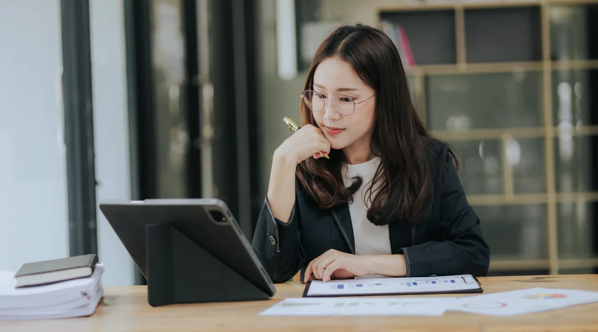 Woman focused on a tablet with graphs and papers on the table