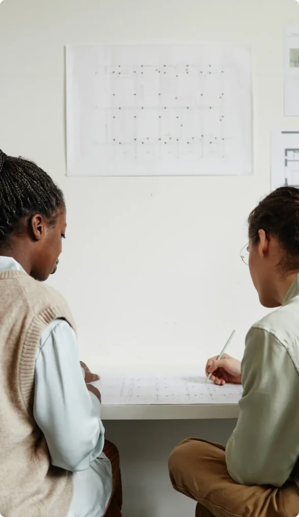 Black woman with braided pony tail wear a brown sweater vest with a white shirt talking to a White male coworker with curly brown hair wearing brown pants and light green shirt sitting in a conference room discussing using LegalZoom for their business dissolution.