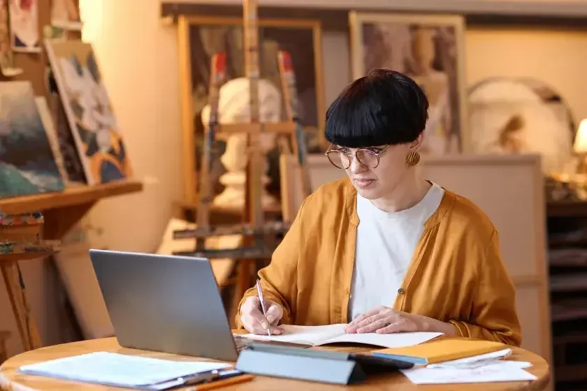 Young entrepreneur in her art gallery, seated at her work station and working on her laptop to  take notes on how to get a Georgia business license.