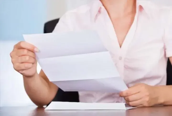 Close up of a woman sitting at a desk reading a piece of mail.
