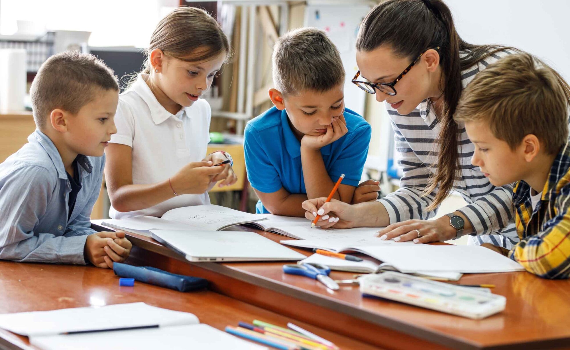 An image of a teacher writing on a book and teaching her students. 