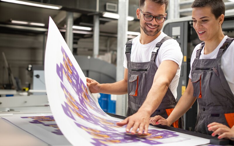 An image of 2 people holding a cardboard paper and discussing in a workshop.