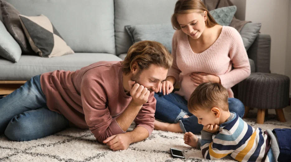 A joyful family, including an expecting mother, laughing and relaxing together in a cozy living room, relieved after creating their joint last will and testament.