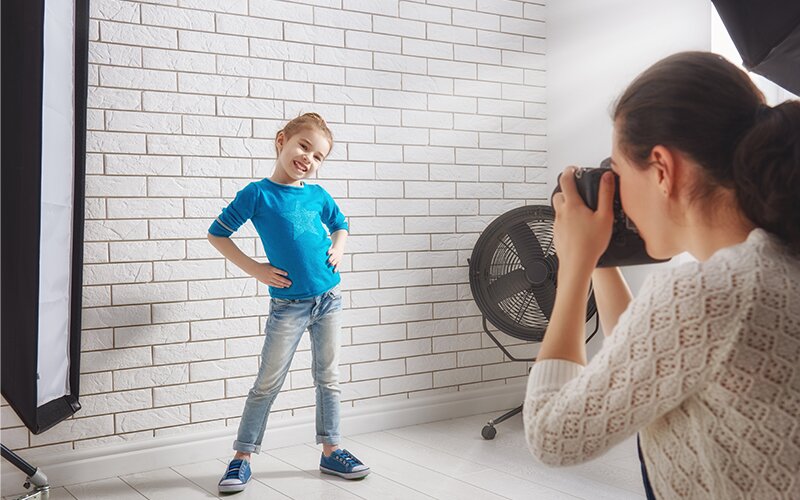 An image of a kid posing for the photographer in a studio.