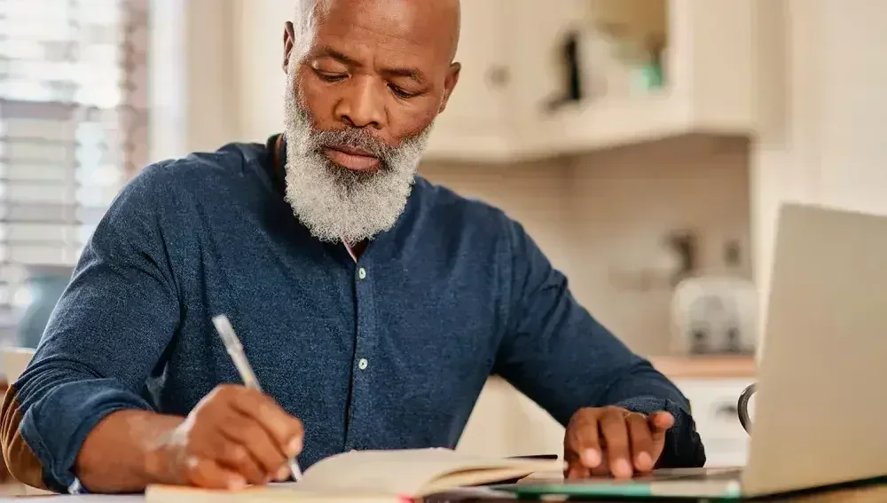 A man sits at his desk and writes out terms for his estate plan and last will.