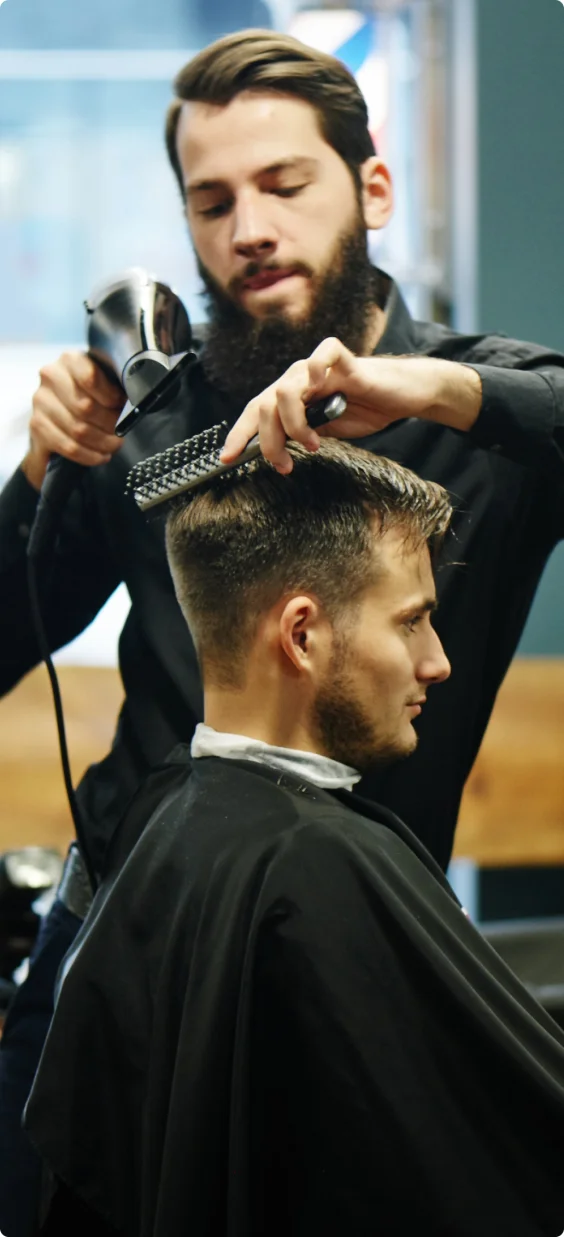 a hair stylist uses a blow dryer and brush for his client in a barber shop.