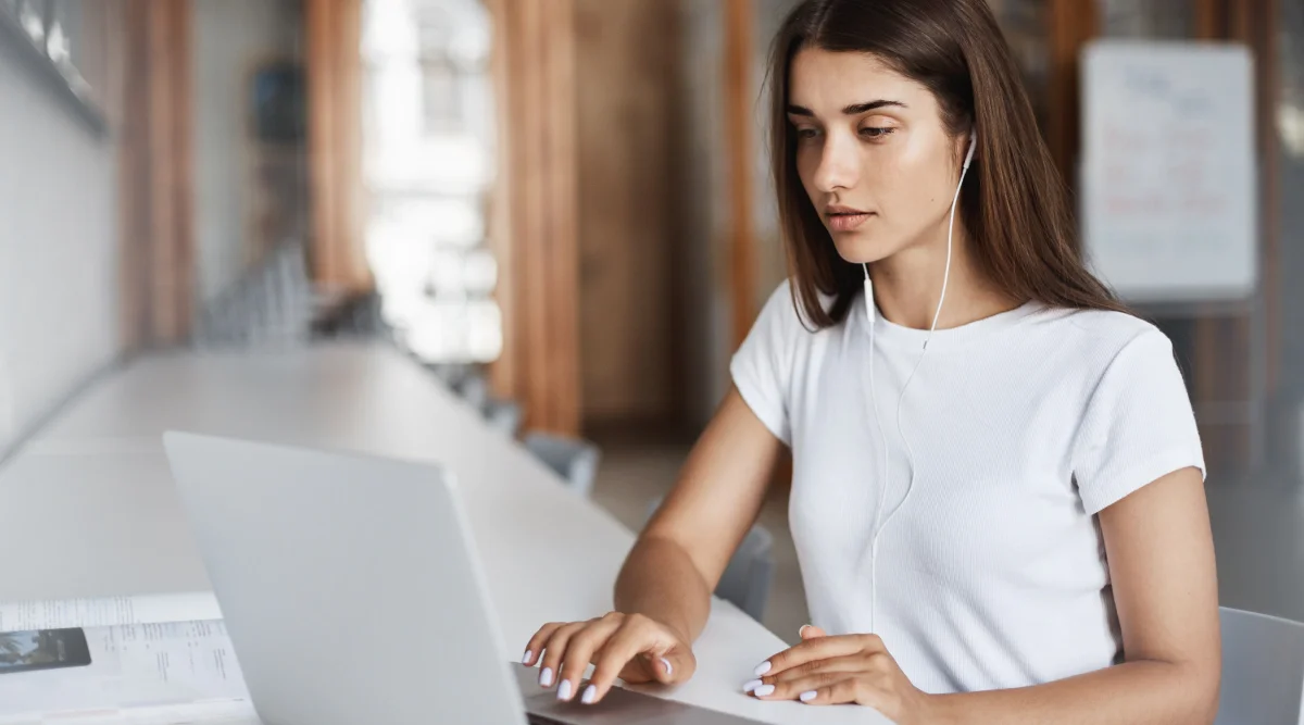 Woman with headphones focused on a laptop in a library