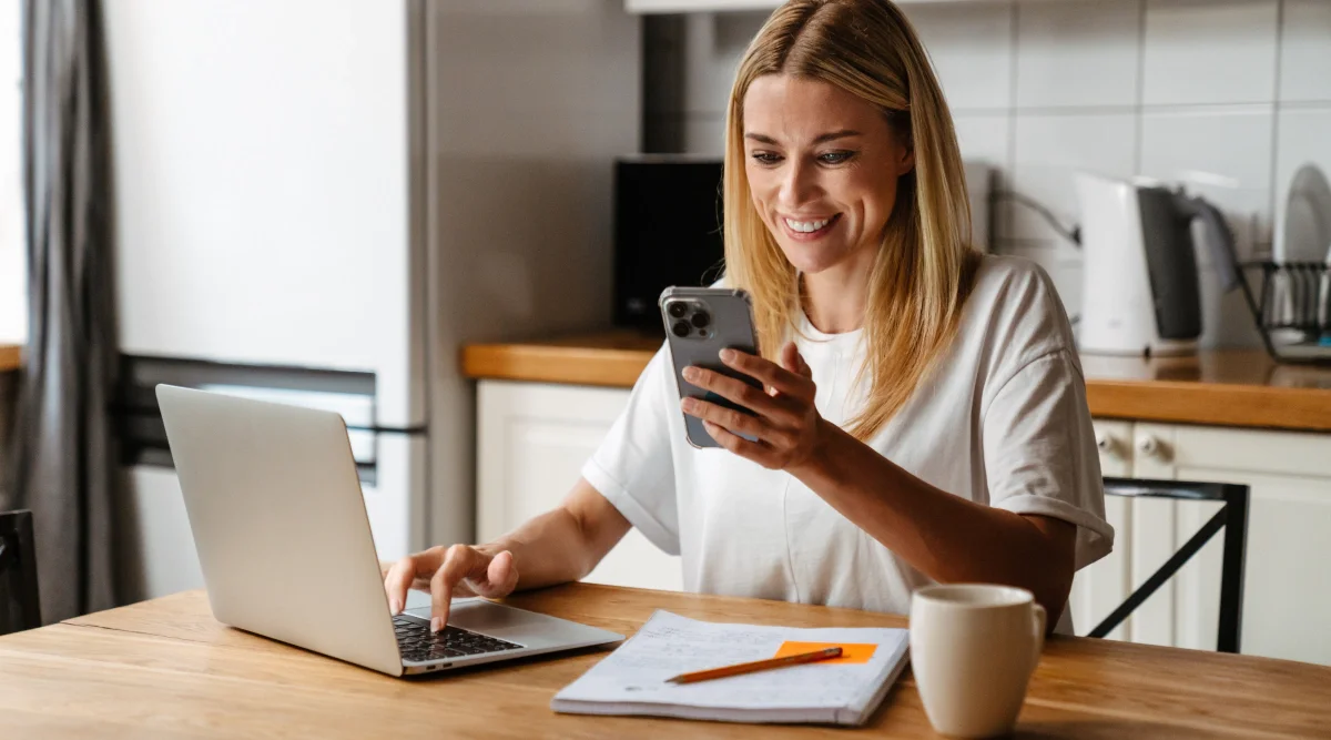 Woman smiling at phone while using a laptop