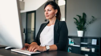 Woman typing on a desktop computer in a bright office