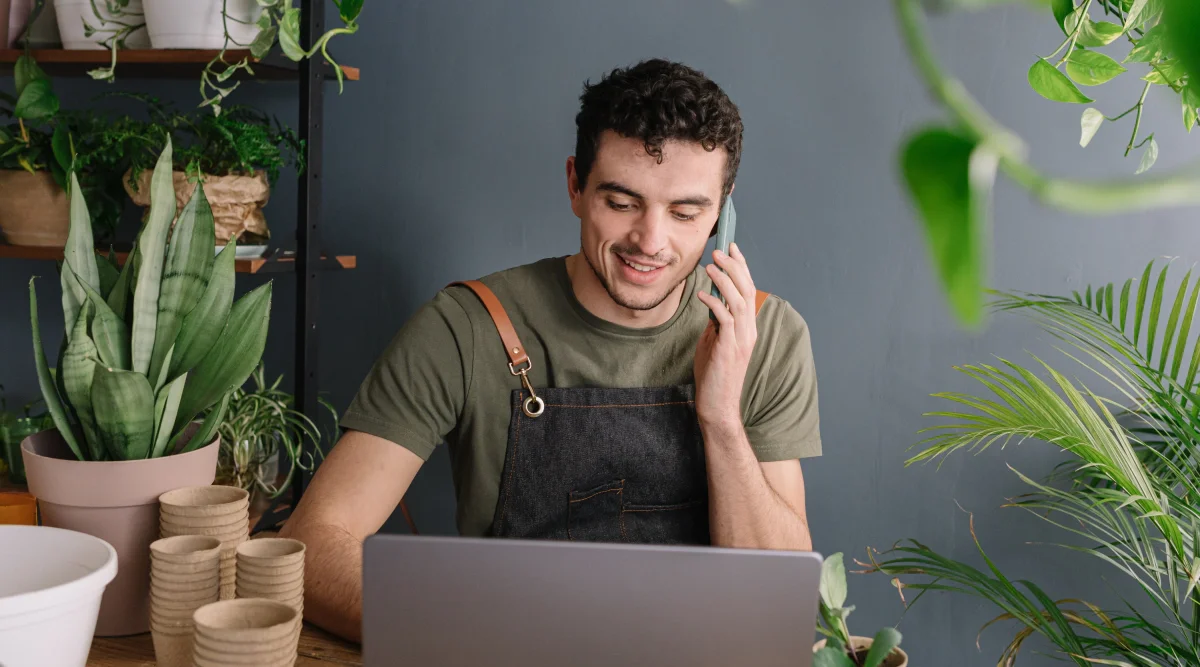 Man in apron on phone surrounded by plants