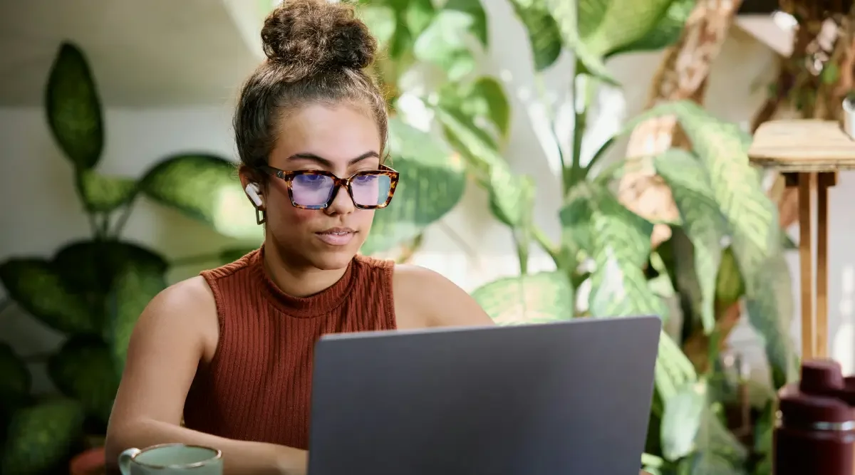 A woman sits at a desk and does a trademark search on her laptop computer.