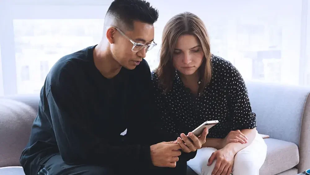 Two people on a living room couch are reading step-by-step instructions on creating a pet trust.