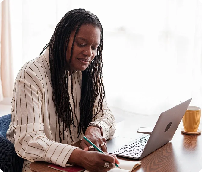 A woman in front of the desk writing in the notebook