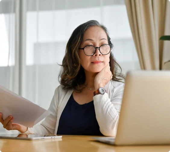 A woman wearing glasses sits at her computer thoughtfully.