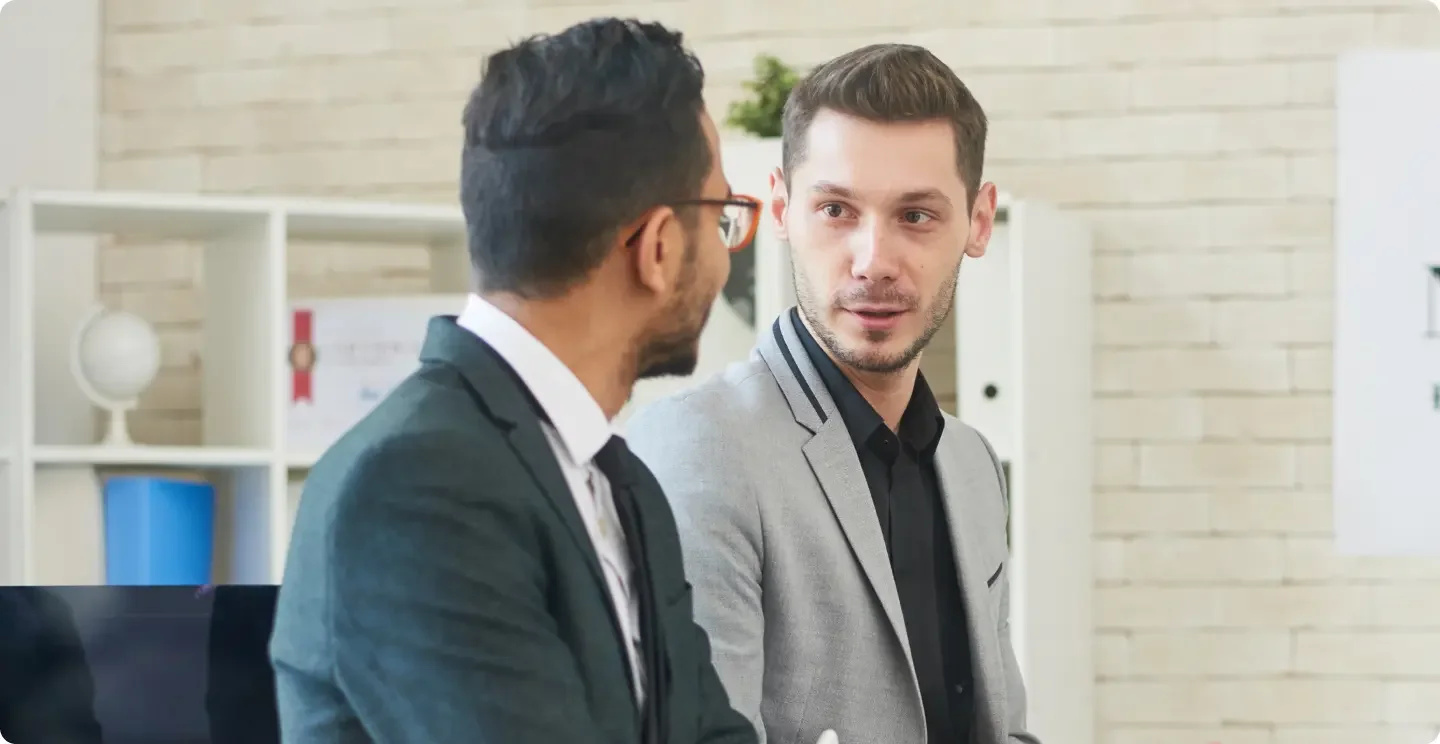 Man wearing a grey suit with a black shirt talking to a male coworker in a black suit with white shirt and black tie discussing doing their business dissolution with LegalZoom.