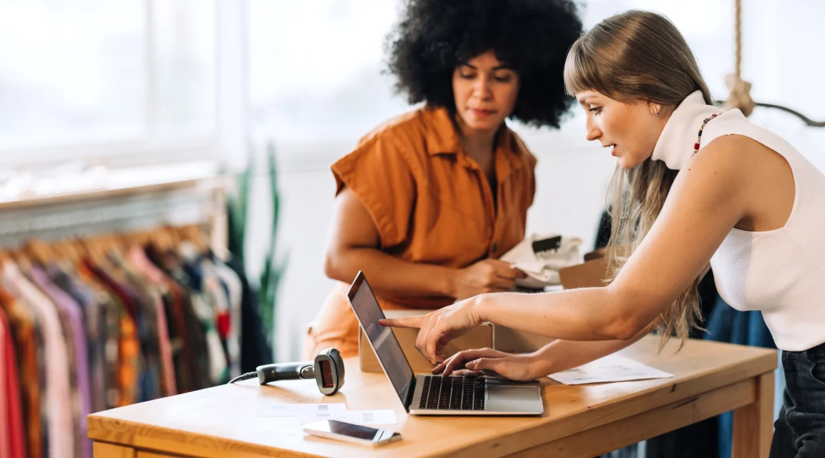 Retail setting, two women working on a laptop, surrounded by clothes