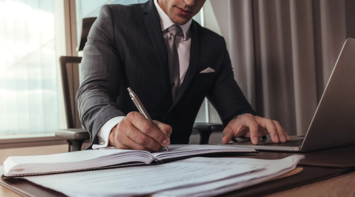 A man in a business suit takes notes in a notebook