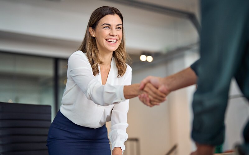 An image of a happy lady shaking hands with a man inside an office.