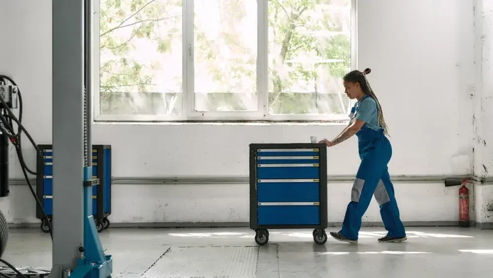 A woman in overalls pushes a tool cart in a warehouse