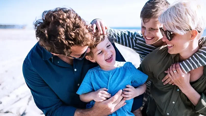 Young family with two small children laughing outdoors on beach, having fun.